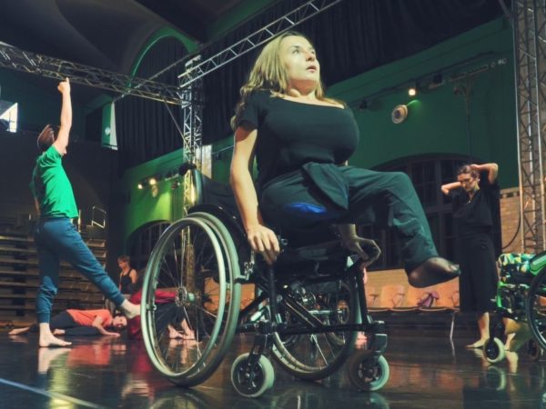 A female performer raises herself up from her wheelchair