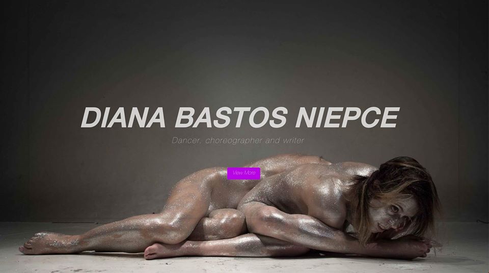 A nude female performer lies on the ground, covered in silver glitter