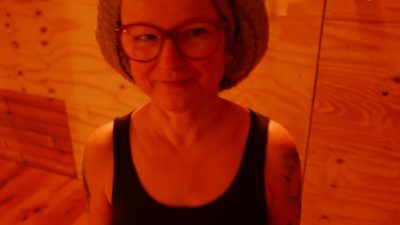 A woman with a knitted beanie hat, black top and glasses smiles