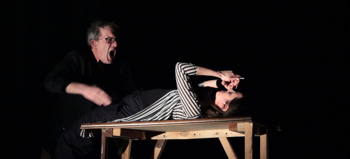  The performance is based on human trafficking . In this photo we see the situation where the woman who is being trafficked is being shouted at . She lays on a table with her hands held over her face  