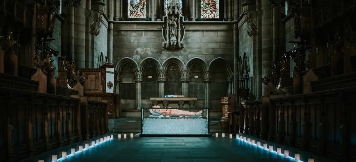 At the altar of a church a woman lies on an open tank of ice 