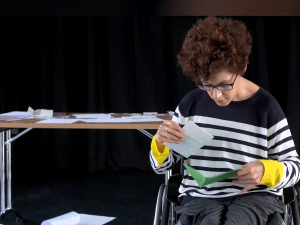 A female performer in a wheelchair sifts through an abundance of letters