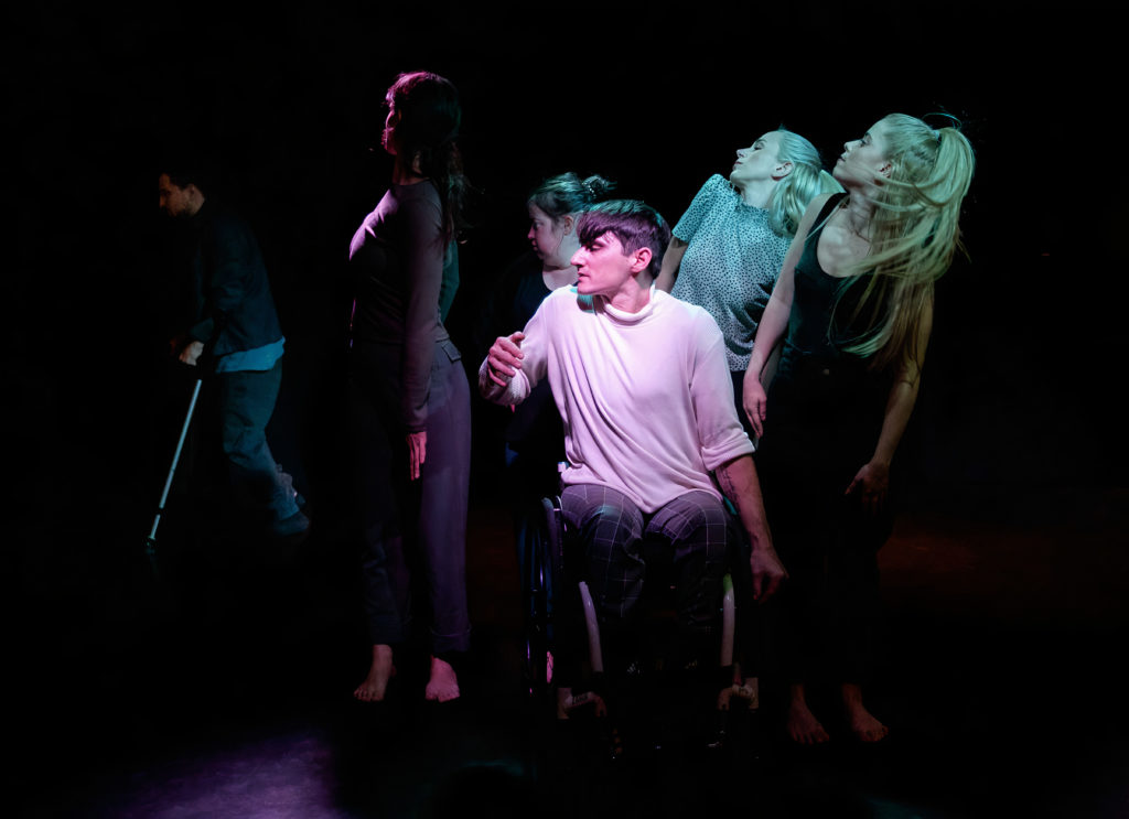 Group of six white dancers, one of them a wheelchair user all turning expressively to one side.