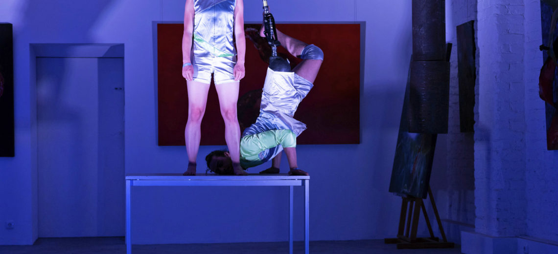 Two dancers, which look like cyborgs, on a table. A women and a man with a leg prosthesis.