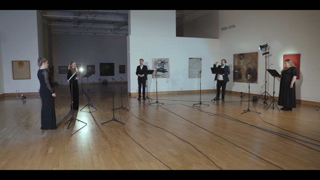 5 white classical singers in black attire perform in a gallery setting