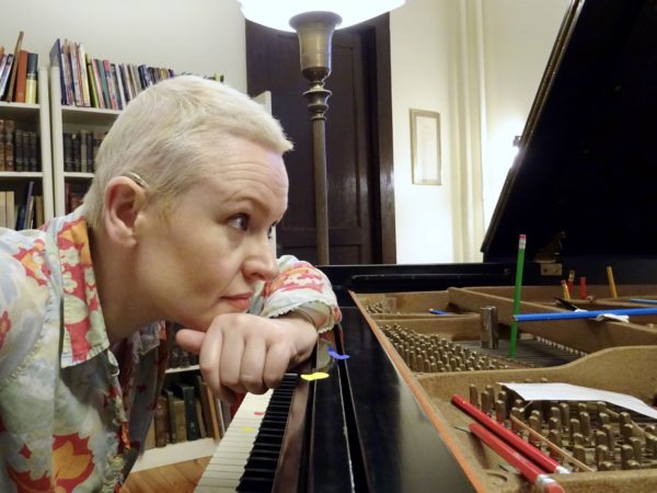 White female with short blonde hair looking into piano