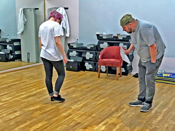 Two people in a rehearsal studio. James Paddock (Artist) in a grey t-shirt and Amber Weyman (performer) with pink hair..