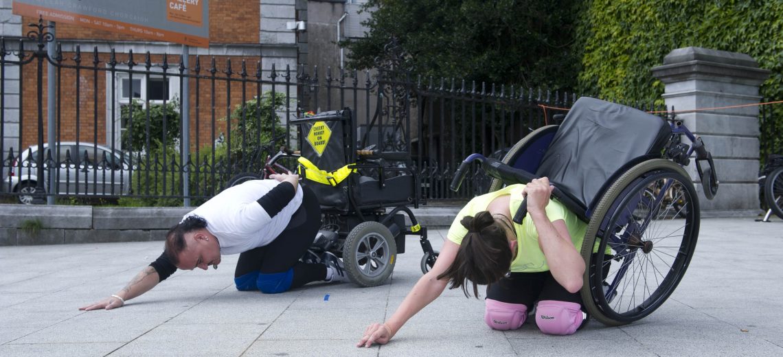 Two wheelchair dancers kneel in a street performance