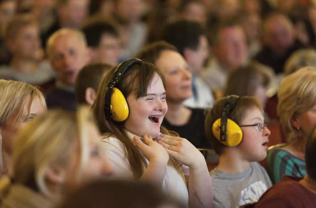 Photograph of a theatre crowd, some of whom are learning disabled and wearing ear defenders