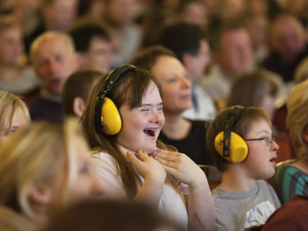 Photograph of a theatre crowd, some of whom are learning disabled and wearing ear defenders