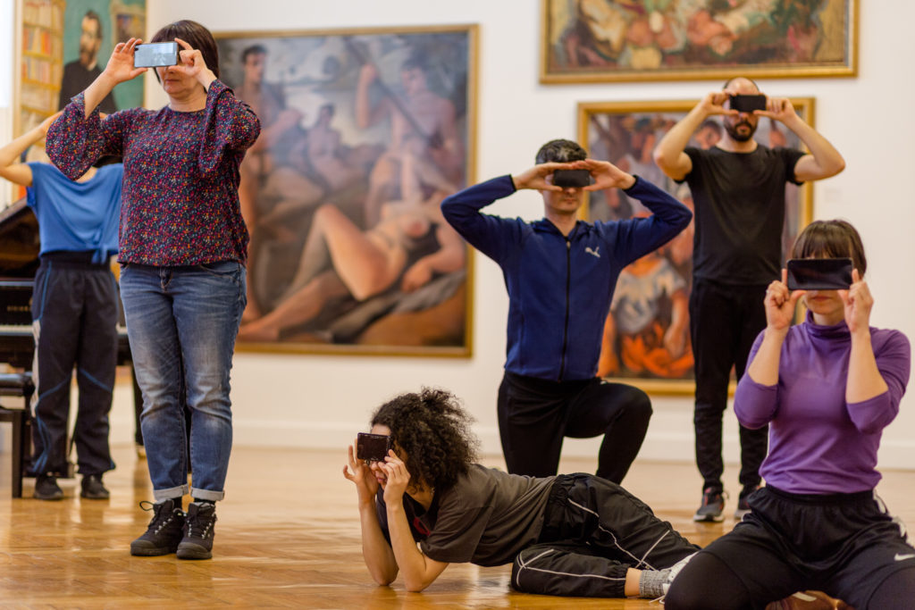 A group of performers pose with their camera phones covering their eyes.