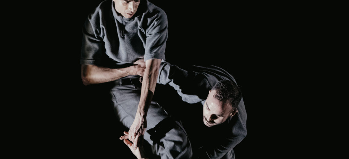 An entanglement of limbs as two male performers cross their arms between each other