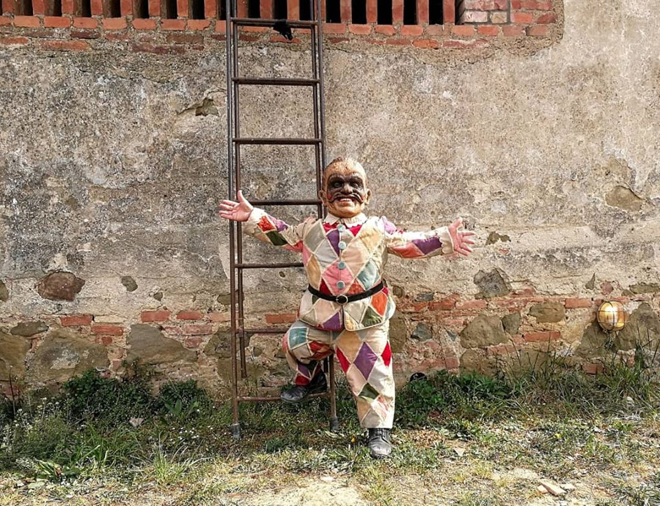 A man of short stature wearing a mask and colourful costume stands against a wall