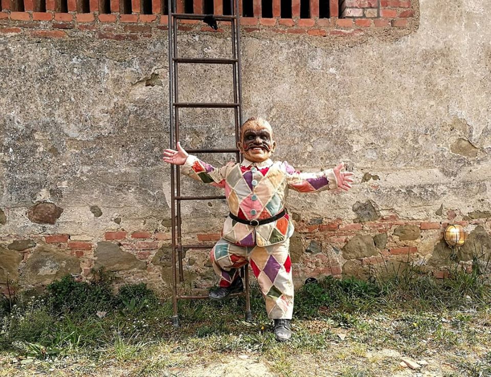 A man of short stature  wearing a mask and colourful costume stands against a wall