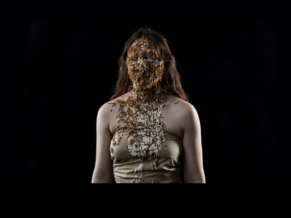 A white female performer with her face covered in white substance and lots of worm-like objects