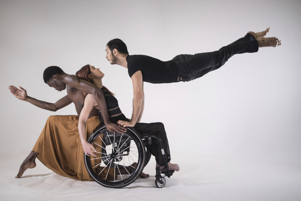 Three dancers in wheelchairs perform acrobatics on stage.