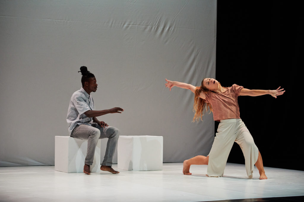 Two dancers on stage. One of them (woman) defying the laws of gravity with her movement.