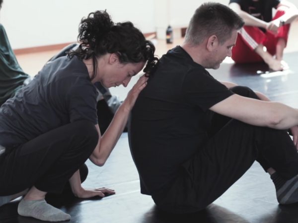 Two dancers sitting on the floor. One of them (male) is turning his back to the other dancer (female).