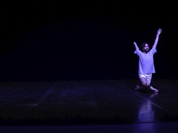 A male dancer with one arm kneels on stage