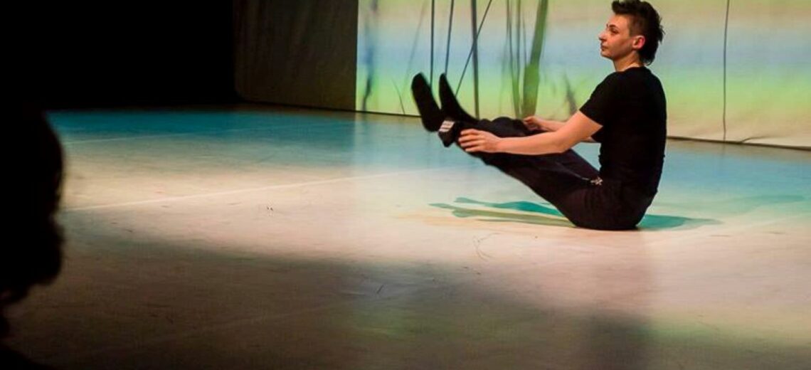 A performer sits on the ground, elevating her legs with her toes pointed