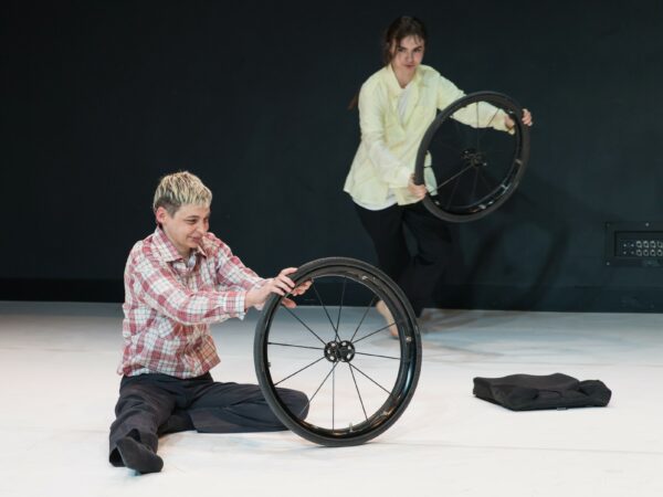 A performer deconstructs her wheelchair and rolls one wheel on the ground.
