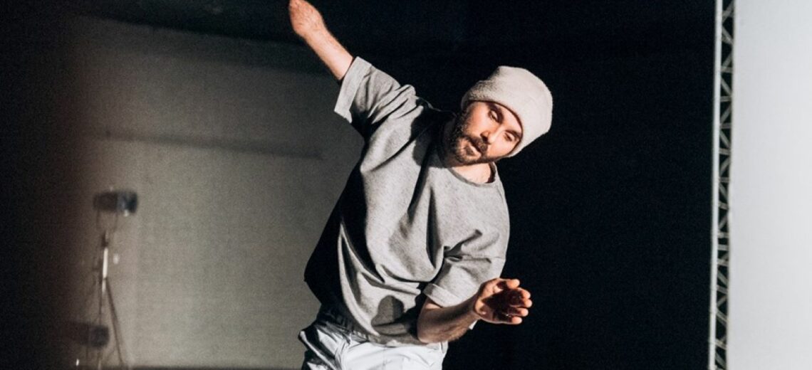 A dancer with one arm moves fluidly wearing casual clothing