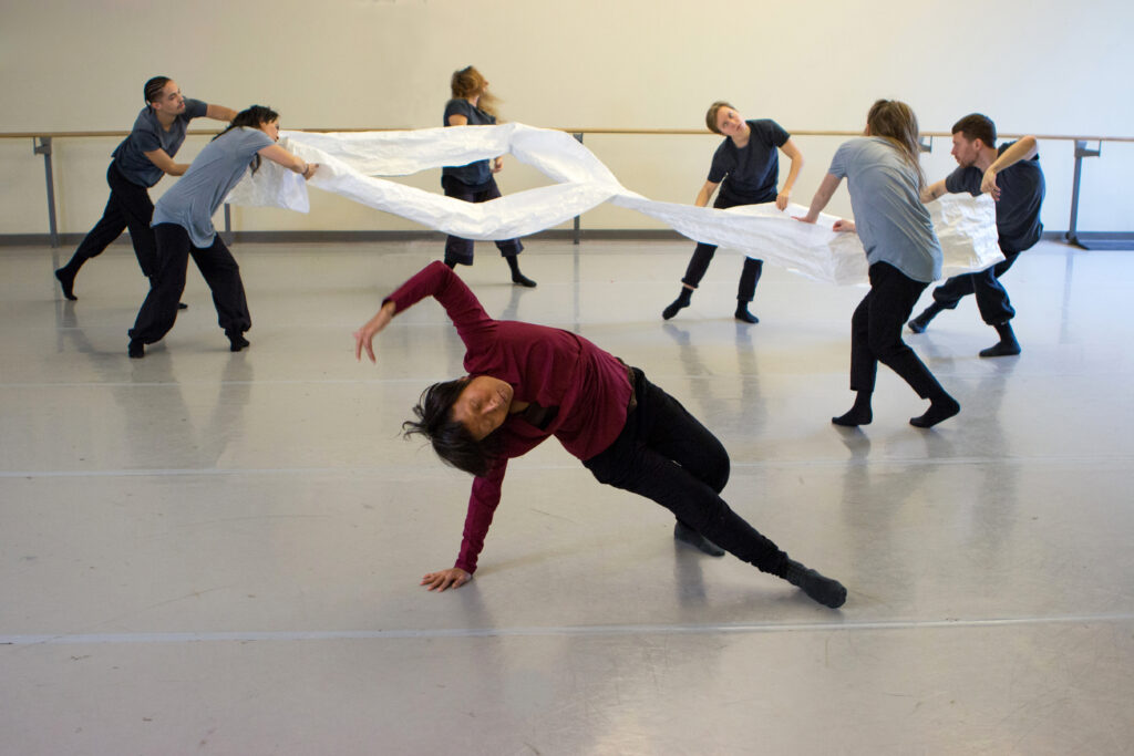 A group of dancers move expressively whilst holding on to a white piece of material