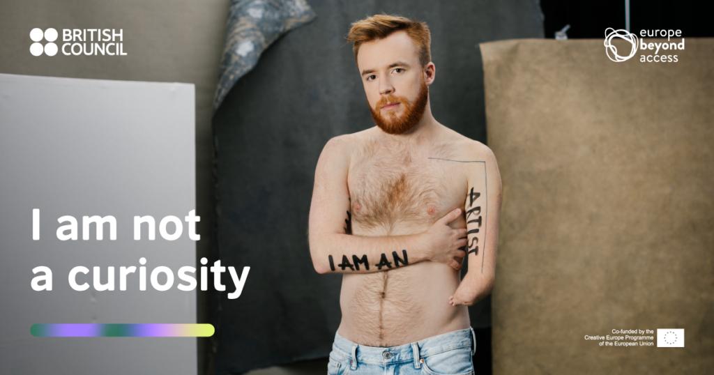A male artist with one hand, shirtless, has 'I am an artist' written across his arms.