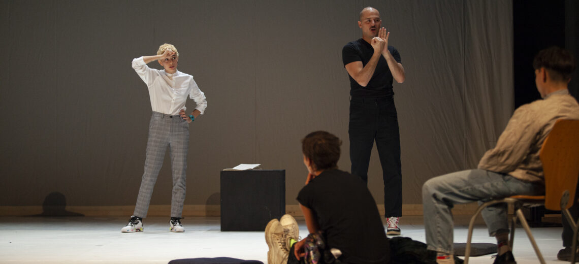 Diana Anselmo stands in a white top and grey trousers on stage.