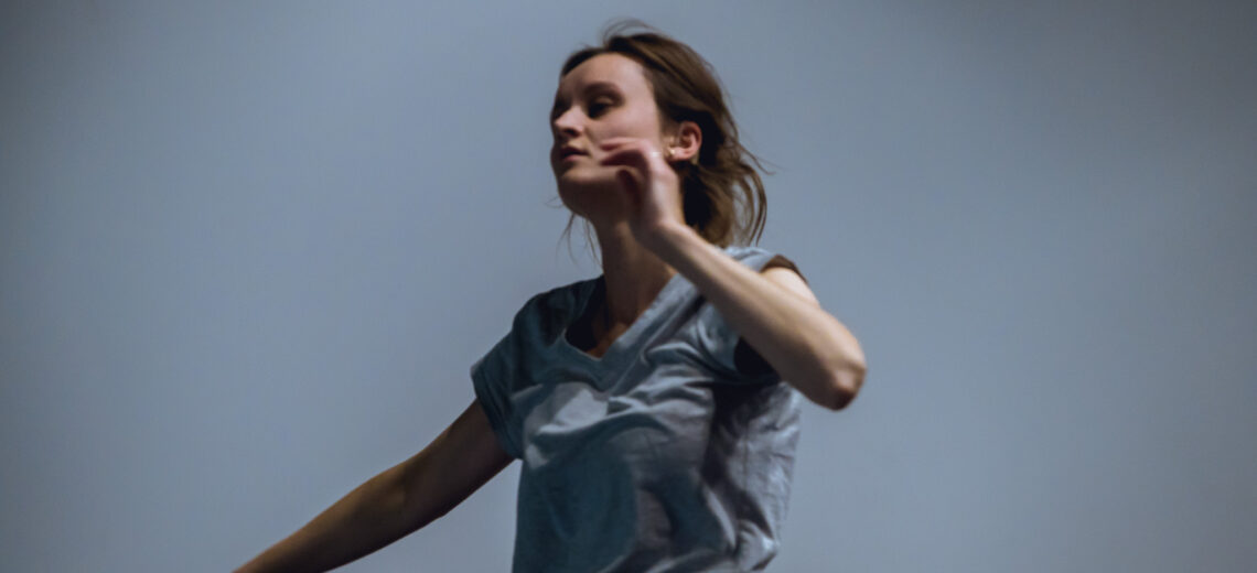 A white Deaf female performer against a soft grey background