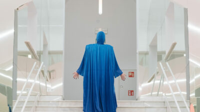 A male performer in a hooded sky-blue cape with hood.