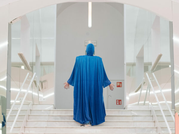 A male performer in a hooded sky-blue cape with hood. 