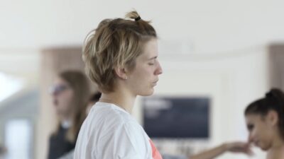 A white woman with short hair stands with her eyes closes in a dance class