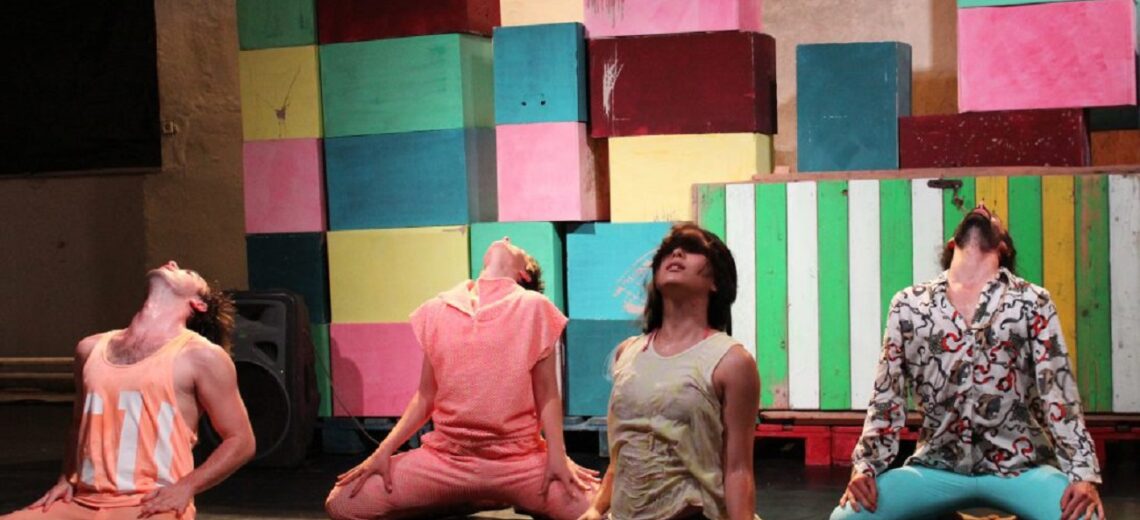 Performers in front of colourful building blocks submit their gaze to the sky