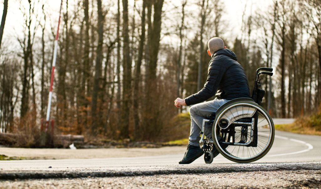 A white male in a wheelchair looks away in a forest