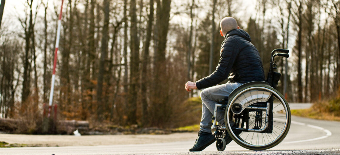 A white male wheelchair user looks away in a forest