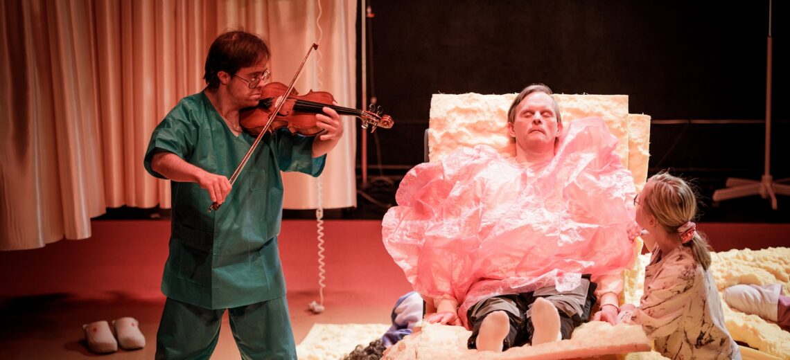 A doctor plays a violin to a person in a hospital bed who is covered in a pink billowing shroud