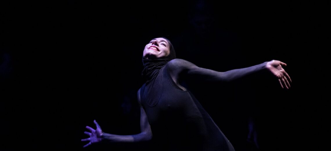 A white female dancer clad in black sways her body upwards with joy and sensuality