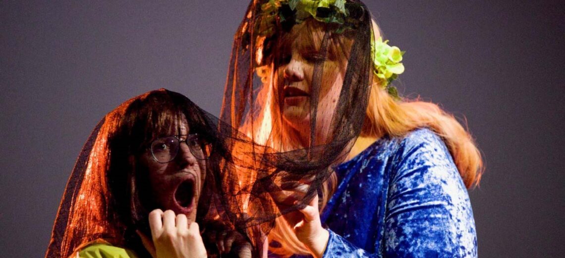 Two white female learning disabled performers in black veils, one appears to scream