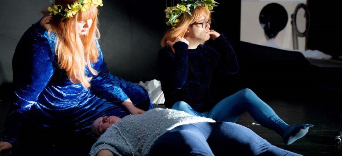 Two female performers appear to watch something off-screen, with flowers in their hair