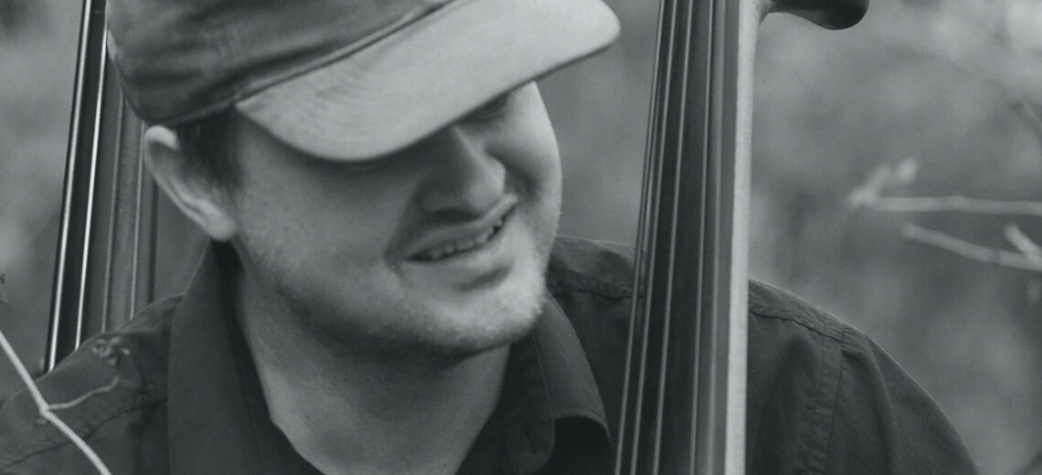 Richard Andersson, a white man wearing a cap with his double bass and another double bass in the background 