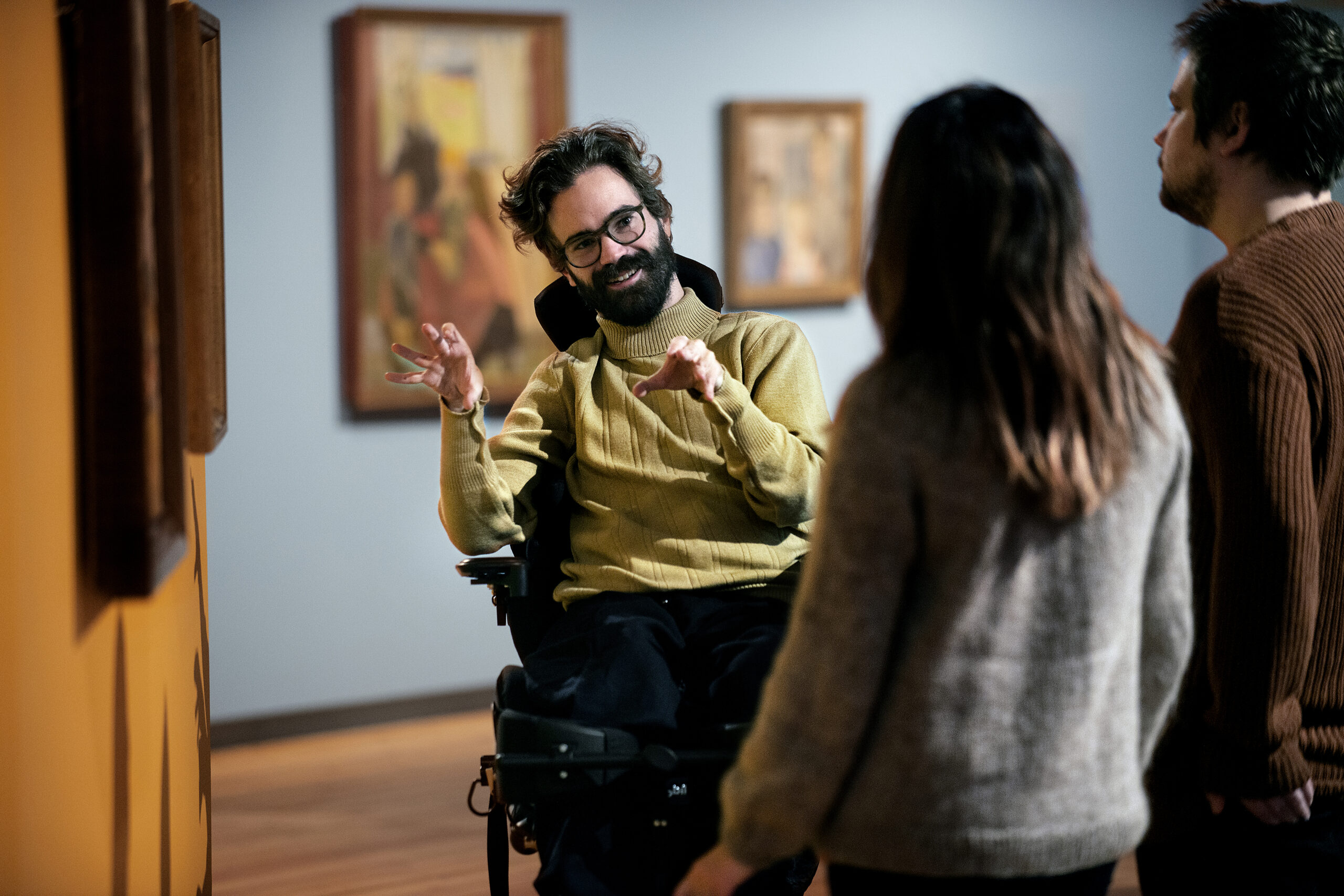 Disabled man in a wheelchair talking to two people in a gallery setting