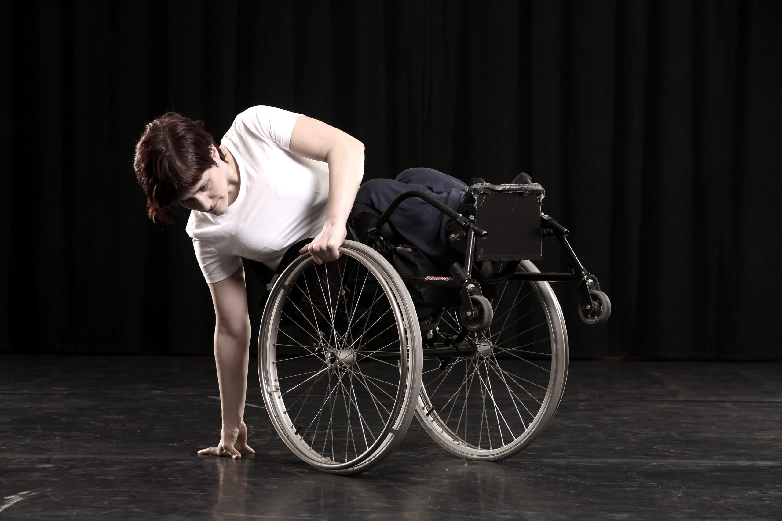 White female wheelchair dancer leans back on her back wheels