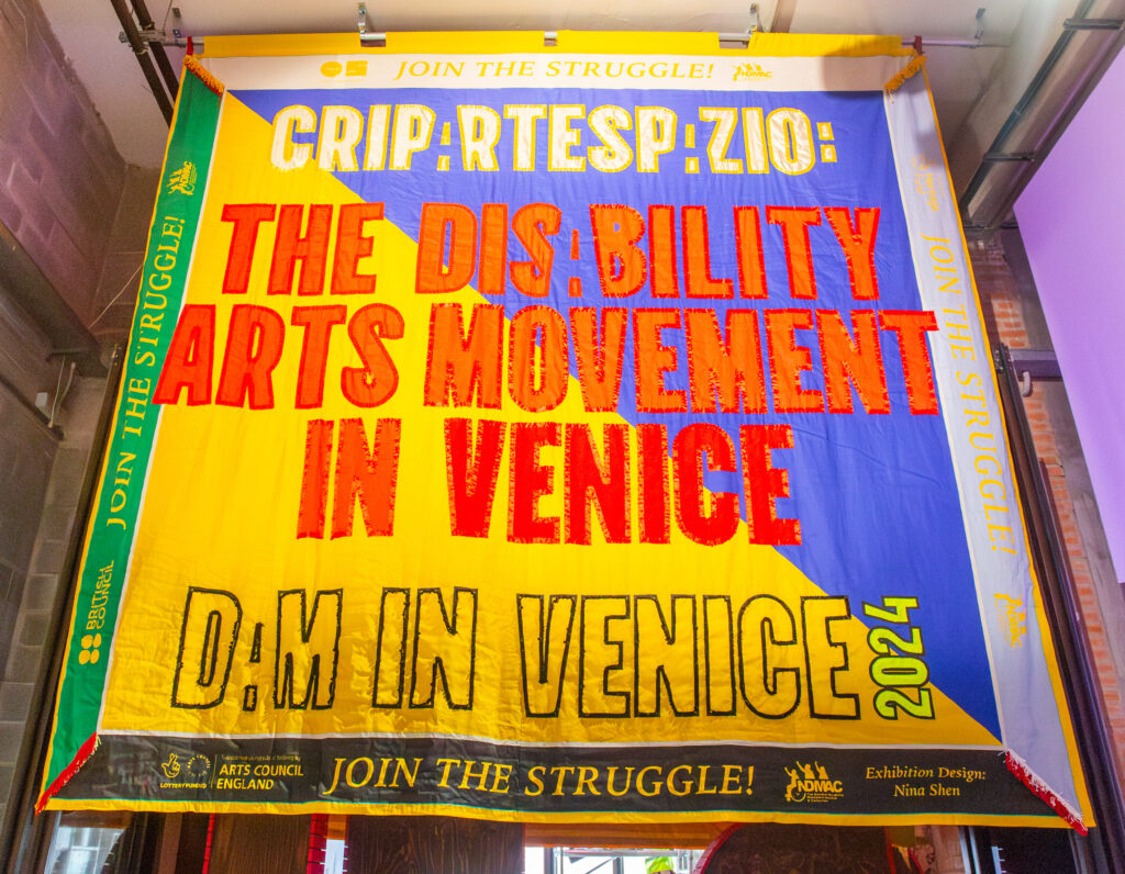 A large colourful protest style banner which reads the disability arts movement in Venice