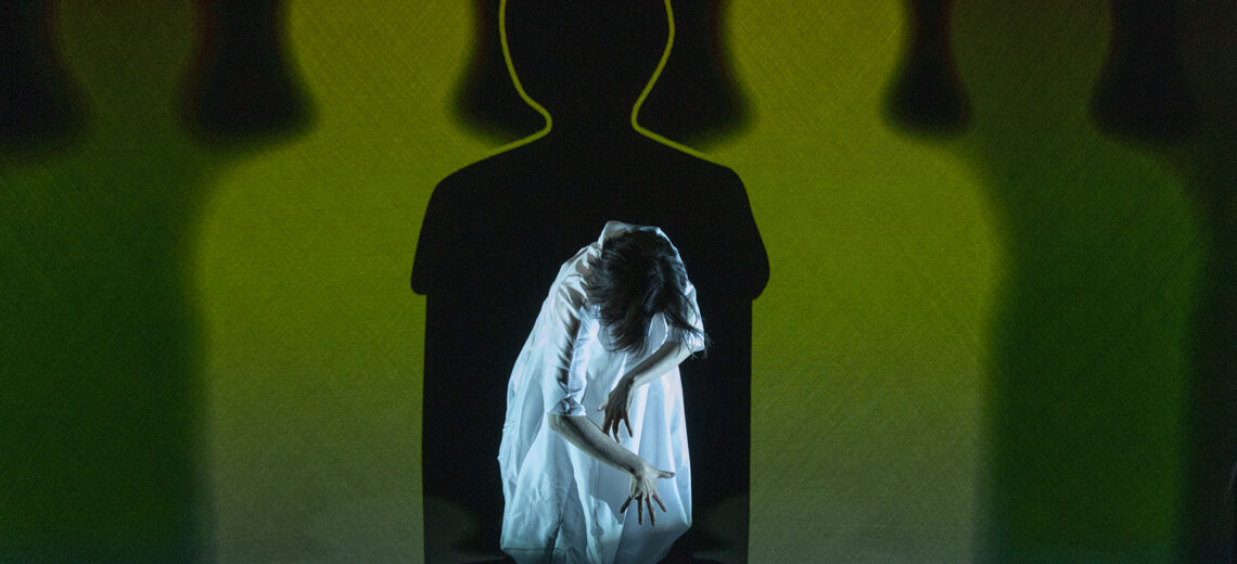 Chisato stands hunched centre stage, head down, fingers splayed. Behind her on the screen is her silhouette, overlapping and repeated in different shades of vibrant green.
